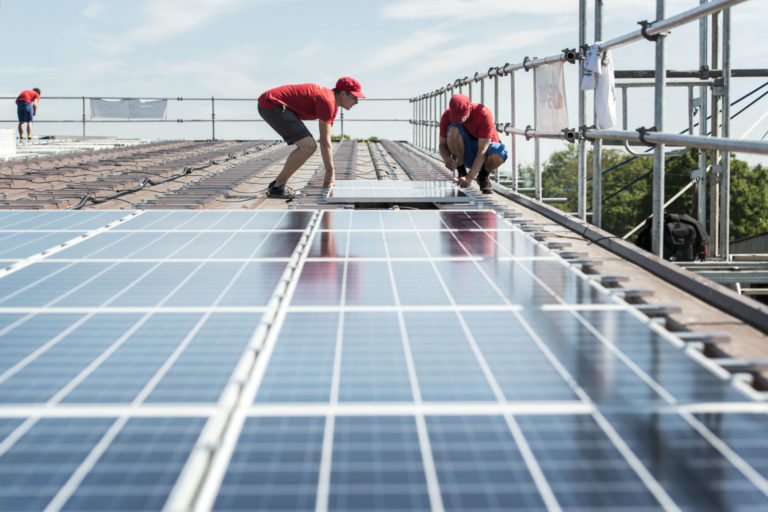 Zwei Männer montieren Solarkollektoren auf einem Dach.