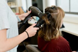 Une coiffeuse sèche les cheveux d'une cliente avec une brosse ronde.