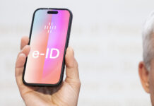 Öffentliche e-ID wird unabhängig von Tech-Konzernen Ein Mann hält ein Smartphone hoch, auf dessen Bildschirm gross ‹e-ID› steht. Die Darstellung symbolisiert die geplante elektronische Identität der Schweiz