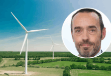 Bruno Tobback: «Der ‹Green Deal› ist auch eine Unabhängigkeitserklärung» Luftaufnahme einer weitläufigen, grünen Landschaft mit zwei großen weissen Windrädern unter einem klaren blauen Himmel. Oben rechts ist ein kreisförmiges Bild überlagert, das das Gesicht von Bruno Tobback, einem Mann mittleren Alters zeigt, der in die Kamera blickt, kurze Haare hat und einen leichten grauen Bart trägt.