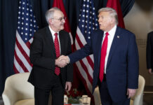 Trump-Deal nach Zoll-Entscheid: Verhandlungen haben schweren Stand Zwei Männer, Guy Parmelin und Donald Trump, in Anzug und Krawatte geben sich vor mehreren Flaggen (USA und Schweiz) die Hand. Der eine trägt ein dunkelblaues Sakko mit roter Krawatte, der andere einen dunklen Anzug mit gemusterter roter Krawatte. Im Hintergrund stehen zwei weiße Sessel und ein kleiner Tisch mit Blumenarrangement und Wassergläsern.