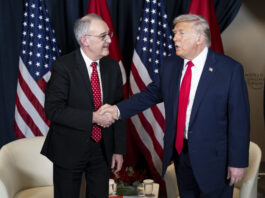 Trump-Deal nach Zoll-Entscheid: Verhandlungen haben schweren Stand Zwei Männer, Guy Parmelin und Donald Trump, in Anzug und Krawatte geben sich vor mehreren Flaggen (USA und Schweiz) die Hand. Der eine trägt ein dunkelblaues Sakko mit roter Krawatte, der andere einen dunklen Anzug mit gemusterter roter Krawatte. Im Hintergrund stehen zwei weiße Sessel und ein kleiner Tisch mit Blumenarrangement und Wassergläsern.