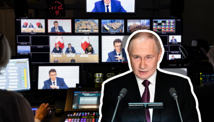 In einer schwach beleuchteten Video-Regie steht im Vordergrund ein Multimedia-Mischpult, dahinter sind mehrere Kontrollmonitore zu sehen, die Aufnahmen einer Medienkonferenz des Bundesrats zur Anti-SRG-Initiative (Tische, Redner und Schweizer Flaggen) zeigen. Darauf überlagert ist Wladimir Putin, ein Mann in dunklem Anzug und Krawatte, der hinter einem Pult mit zwei Mikrofonen steht und offenbar zu einem Publikum spricht.