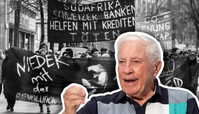 blochsafrika Composite montrant une photographie historique en noir et blanc d'une manifestation avec des banderoles en allemand, dont une principale se lisant 'Afrique du Sud : les banques suisses aident à tuer avec des crédits' et une autre 'à bas l'Apartheid' avec un poing levé. Au premier plan, un portrait détouré d'un homme âgé aux cheveux blancs, vêtu d'un polo bleu, qui pointe du doigt vers la scène de manifestation historique en arrière-plan.