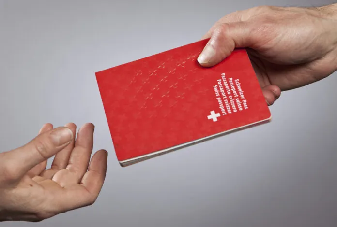 MIGRATION, BUERGERRECHT, SCHWEIZER, SCHWEIZERIN, AUSLAENDER, AUSLAENDERIN, PASS, REISEPASS, NATIONALITAET, NATION, SCHWEIZ, EU, EUROPAEISCHE UNION, DEUTSCHLAND Eine Hand überreicht einen Schweizer Pass an eine dritte, leere Hand, die sich dem Schweizer Pass entgegenstreckt.